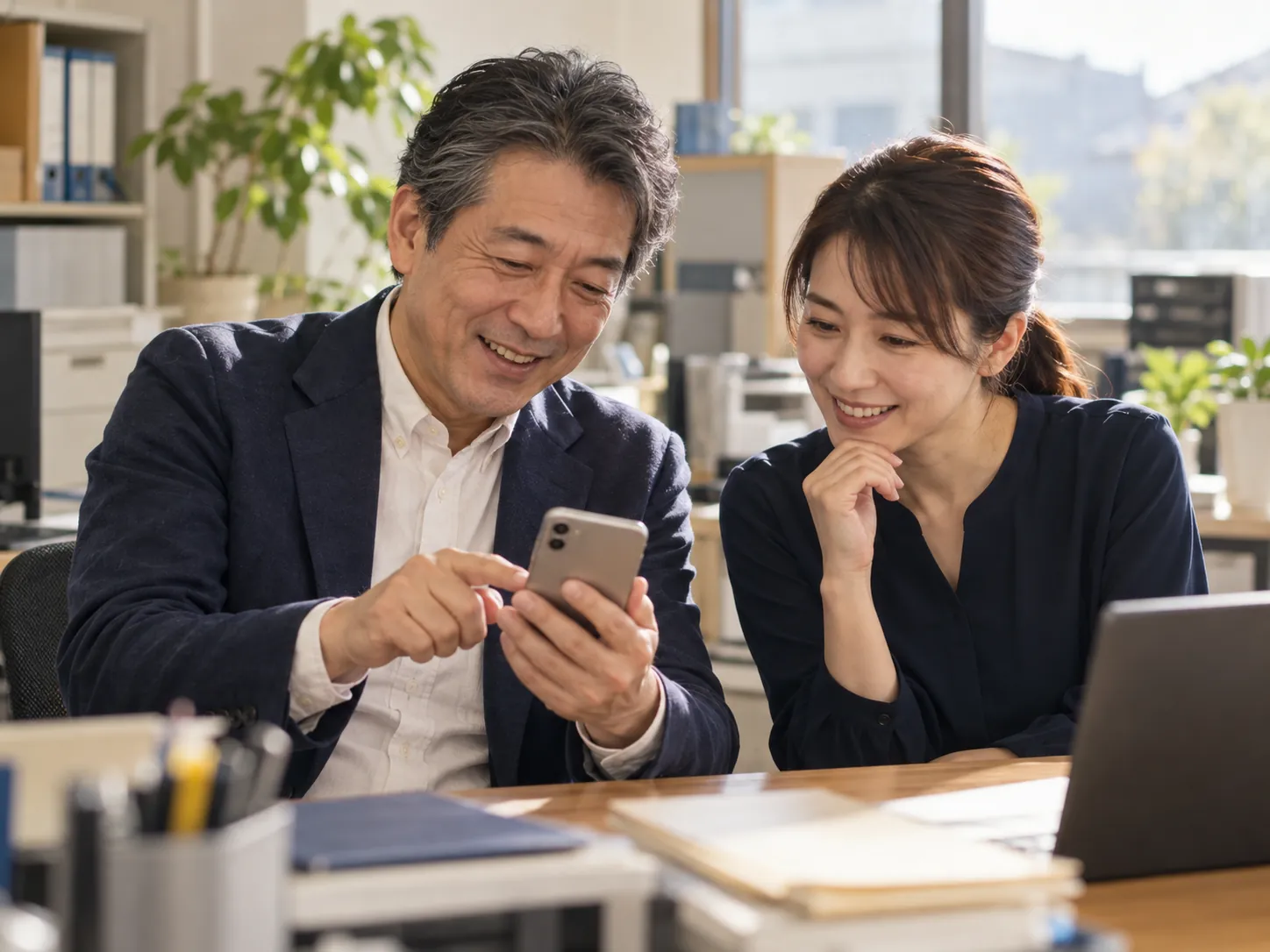 社長と事務の担当者がスマホをのぞいて笑う場面（イメージ）